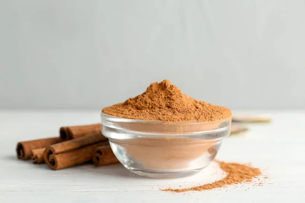 Bowl with aromatic cinnamon powder and sticks on wooden table — Stock Photo, Image