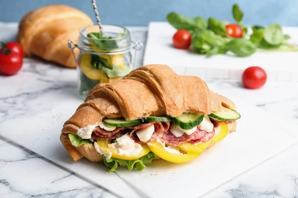 Välsmakande croissant smörgås med salami på bord — Stockfoto