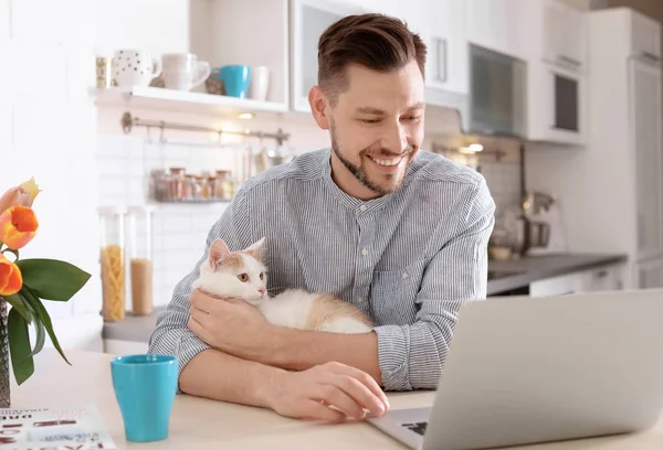 Young man with cute cat and laptop at home