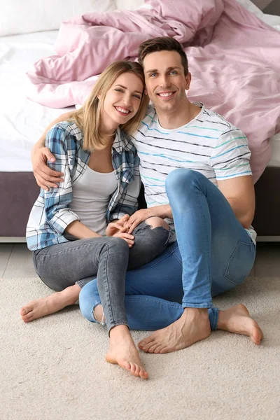 Schönes junges Paar sitzt neben dem Bett auf kuscheligem Teppich zu Hause — Stockfoto