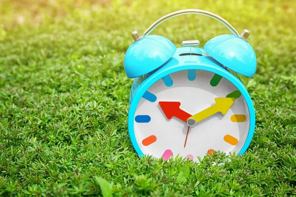 Alarm clock on green plants, outdoors. Time change concept — Stock Photo, Image