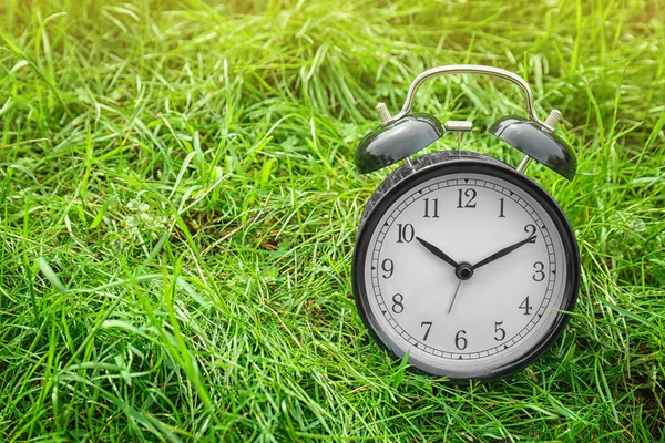 Alarm clock on green grass, outdoors. Time change concept — Stock Photo, Image