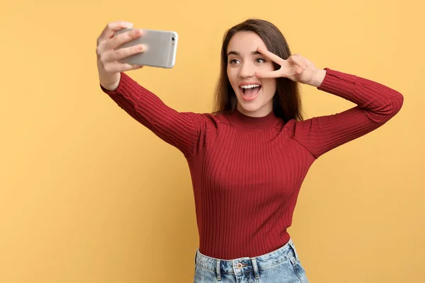 Attraktive junge Frau macht Selfie mit Handy auf farbigem Hintergrund — Stockfoto