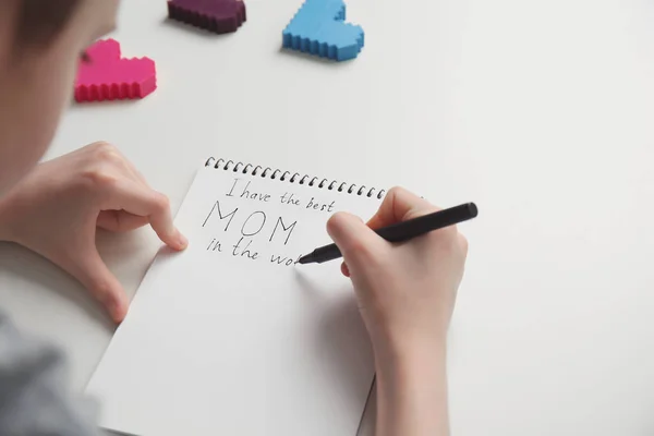 Klein kind schrijven Heilwens voor Mother's Day in notebook op lichte achtergrond — Stockfoto