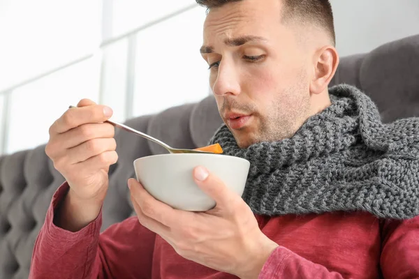 Больной молодой человек ест бульон, чтобы вылечить холод в постели дома — стоковое фото