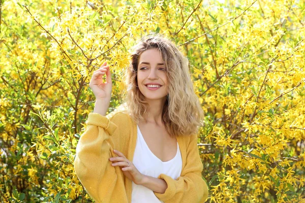 Atractiva joven posando cerca de un arbusto floreciente en el soleado día de primavera —  Fotos de Stock