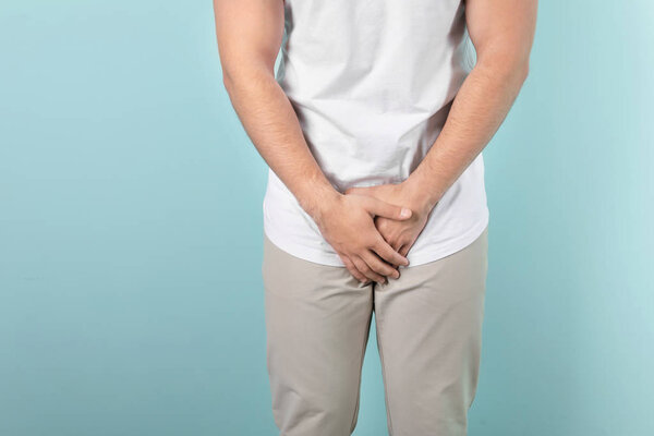 Young man with urological problems suffering from pain on color background