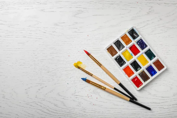 彩色油漆和画笔在木质背景的塑料调色板, 顶部视图 — 图库照片