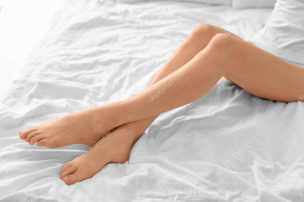 Young woman showing smooth silky skin after epilation on bed at home