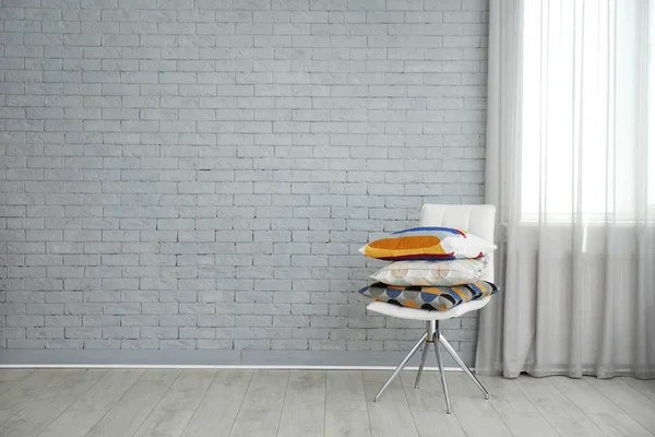 Travesseiros diferentes na cadeira perto da parede de tijolo no quarto — Fotografia de Stock
