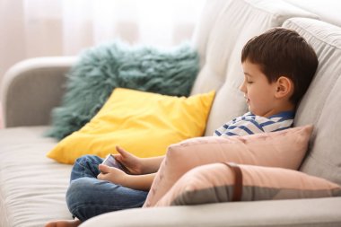 Sevimli küçük çocuk evde kanepe üstünde hareket eden telefon ile