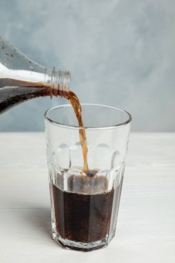 Serinletici gazoz bardağa dökülüyor mavi arka plana karşı beyaz ahşap masaya.