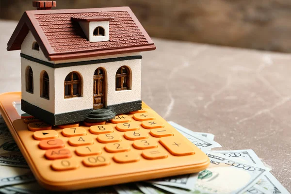 Modelo de casa con calculadora y dinero en la mesa, primer plano. Servicio de agente inmobiliario —  Fotos de Stock