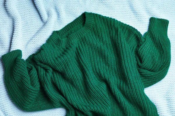 Warm green knitted sweater on light blue blanket, flat lay — Stock Photo, Image