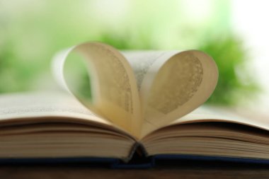 Kalbin ahşap masadaki kitap sayfalarından yapılmış. Arka plan bulanık, yakın plan.