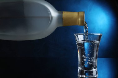 Koyu arkaplandaki shot bardağına mavi ışık ile votka dökülüyor.