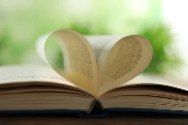 Herz aus Buchseiten auf Holztisch vor verschwommenem Hintergrund, Nahaufnahme — Stockfoto