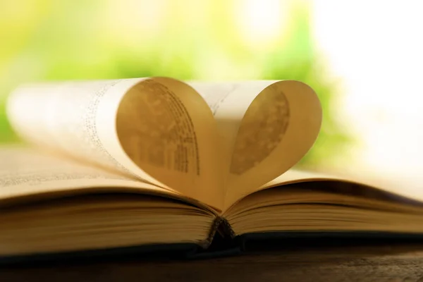 Heart made of book pages on wooden table against blurred background, closeup — Stock Photo, Image