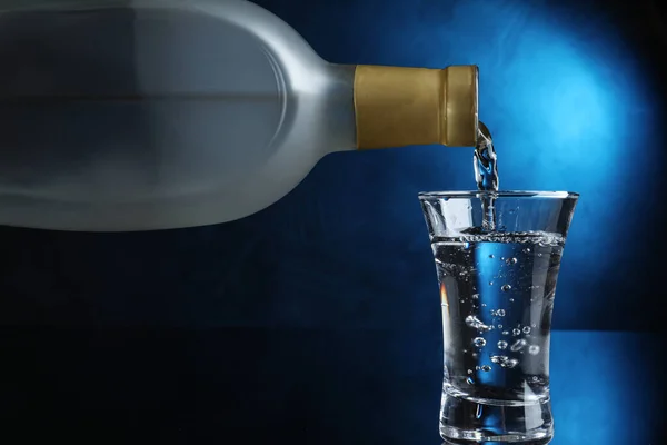 Pouring vodka into shot glass on dark background with blue light