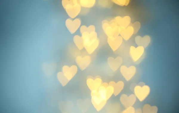 Wazig zicht op mooie gouden hartvormige lichten op lichtblauwe achtergrond — Stockfoto