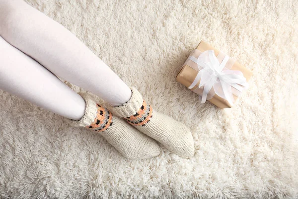 Woman wearing knitted socks on rug, top view. Warm clothes