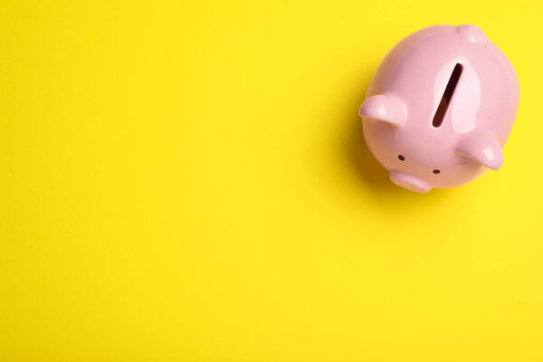 Top view of piggy bank on yellow background, space for text. Money savings