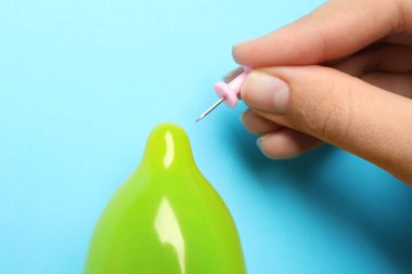Açık mavi arka planda iğneyle şişirilmiş prezervatif delen kadın, yakın plan. Güvenli seks.