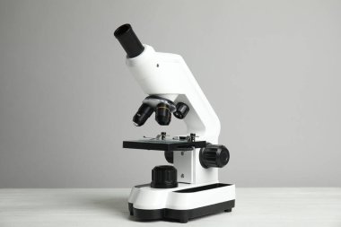 Gri arka plana karşı beyaz ahşap masadaki modern mikroskop. Tıbbi ekipman