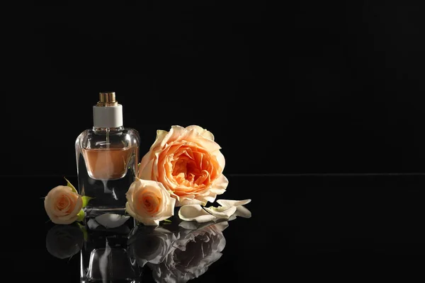 Élégante bouteille de parfum et de belles fleurs sur fond noir. Espace pour le texte — Photo
