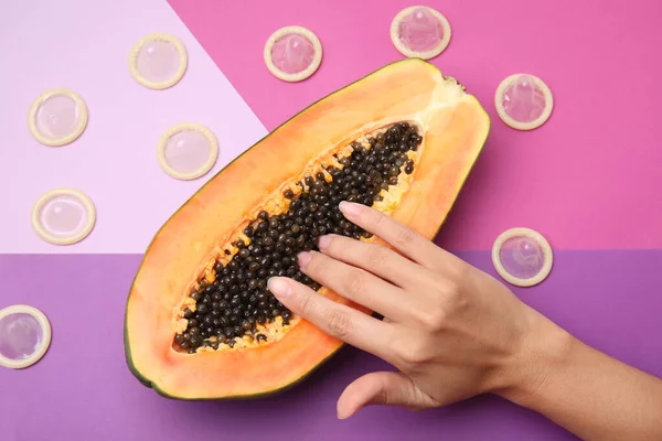 Mujer joven tocando la mitad de la papaya y condones en el fondo de color, vista superior. Concepto de sexo — Foto de Stock