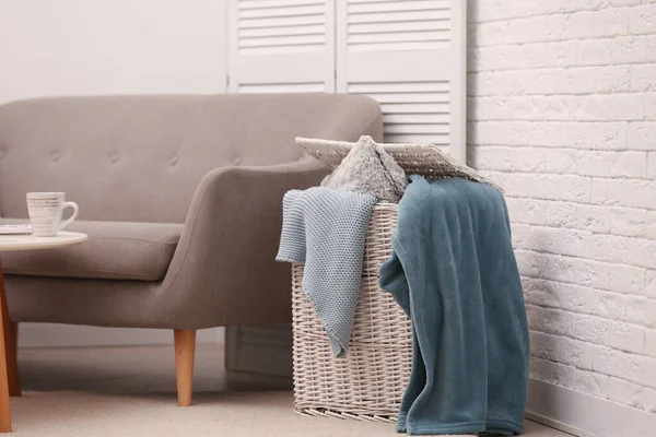 Корзина с одеялами и подушкой возле дивана в помещении — стоковое фото