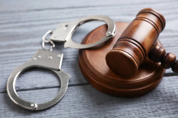 Молоток и наручники на сером деревянном столе, крупным планом. Уголовное право — стоковое фото
