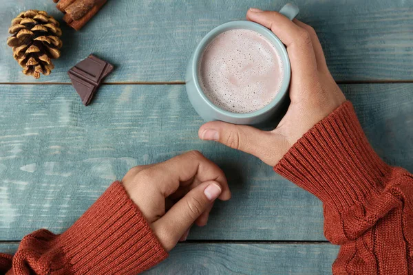 Frau hält Tasse mit köstlichem Kakaogetränk an hellblauem Holztisch, Draufsicht — Stockfoto