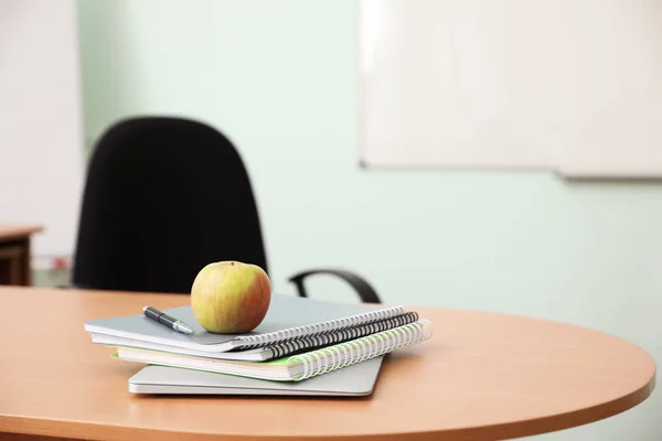 Montón de libros, manzana y portátil en el escritorio del profesor en el aula — Foto de Stock