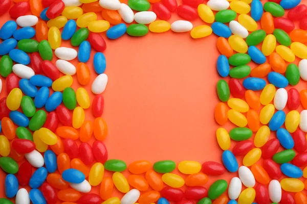 Marco hecho de frijoles de gelatina de colores sobre fondo de coral, disposición plana. Espacio para texto — Foto de Stock