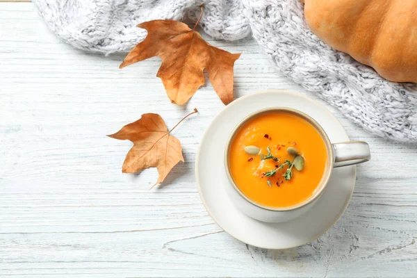 Delicious pumpkin soup in cup on white wooden table, flat lay