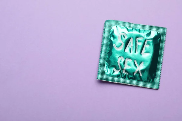 Green condom with phrase SAFE SEX on violet background, top view with space for text — Stock Photo, Image