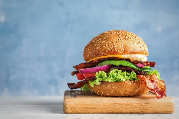 Hambúrguer de bacon suculento fresco na mesa de madeira branca contra fundo azul. Espaço para texto — Fotografia de Stock