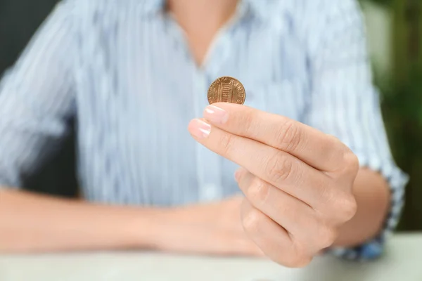 Женщина держит монету за светлым столом в помещении, крупным планом — стоковое фото