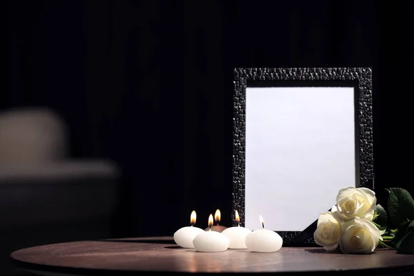 Marco de fotos funerarias con cinta negra, rosas y velas en la mesa de madera en el interior. Espacio para el diseño —  Fotos de Stock