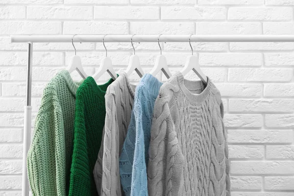 Collection of warm sweaters hanging on rack near brick wall — Stock Photo, Image