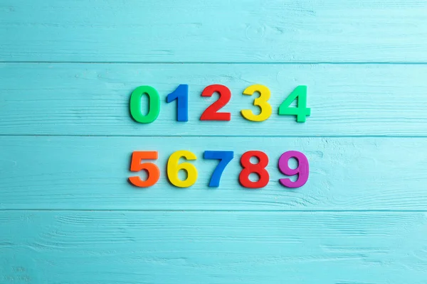 Colorful magnetic numbers on light blue wooden background, flat lay