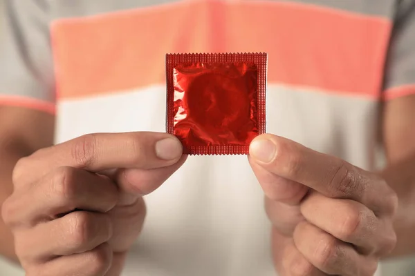 Νεαρός που κρατάει κόκκινο προφυλακτικό, κοντινό πλάνο. Έννοια ασφαλούς σεξ — Φωτογραφία Αρχείου