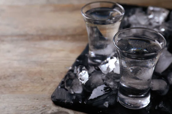 Vodka en vasos de chupito y hielo sobre mesa de madera, espacio para texto —  Fotos de Stock