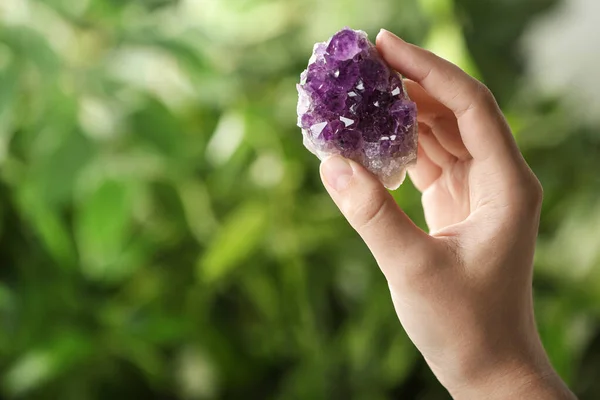 Woman holding beautiful purple amethyst gemstone on blurred green background, closeup. Space for text — Stock Photo, Image