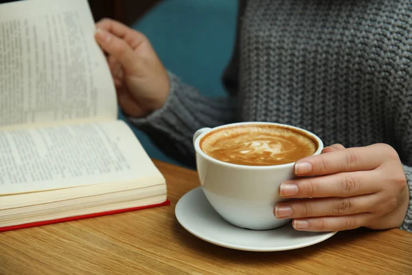 Mulher com xícara de livro de leitura de café na mesa, close-up — Fotografia de Stock