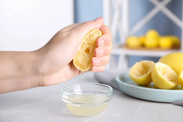 Femme serrant le jus de citron dans un bol en verre à la table de marbre gris, gros plan — Photo