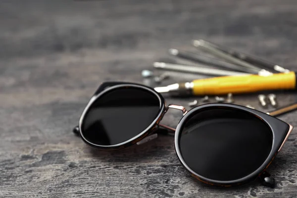 Elegantes gafas de sol femeninas y herramientas de fijación en mesa gris —  Fotos de Stock