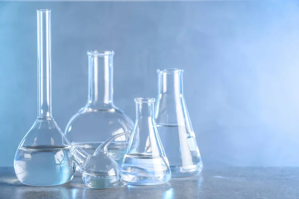 Γυάλινα αντικείμενα εργαστηρίου με υγρά δείγματα για ανάλυση σε γκρίζο τραπέζι με τονισμένο μπλε φόντο — Φωτογραφία Αρχείου