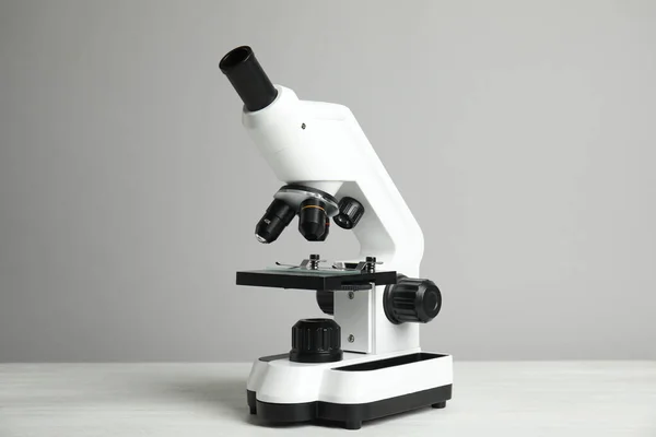 Μοντέρνο μικροσκόπιο σε λευκό ξύλινο τραπέζι με γκρι φόντο. Ιατρικός εξοπλισμός — Φωτογραφία Αρχείου